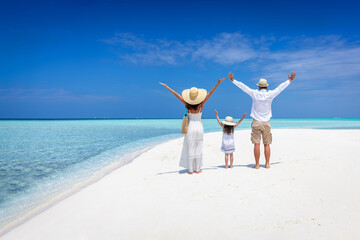 A happy family stands together on a tropical paradise beach with turquoise ocean and white sand during their vacation time
