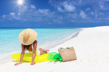 A summer holiday woman with a hat sits on a yellow inflatable at a tropical paradise beach with fine sand and turquoise sea
