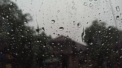 Raindrop on window glass with village trees background. Selective focus