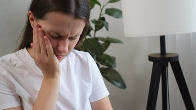 Close up of unhappy young caucasian woman hand touching cheek sit on sofa, face expression from toothache, sensitivity, having tooth or teeth problem, suffering from health. Sensitive teeth concept