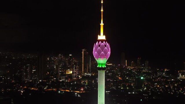 Orbit shot around top of tall TV tower in lotus flower design. Colombo Lotus Tower colourfully glowing into night city. Colombo, Sri Lanka