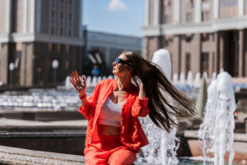Summer portrait of a girl with long blond hair. Girl in orange clothes and sunglasses. The girl turns her head and her hair flutters in the wind.