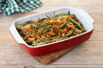 A traditional green bean casserole topped with French Fried Onions and cream of mushroom on wooden table
