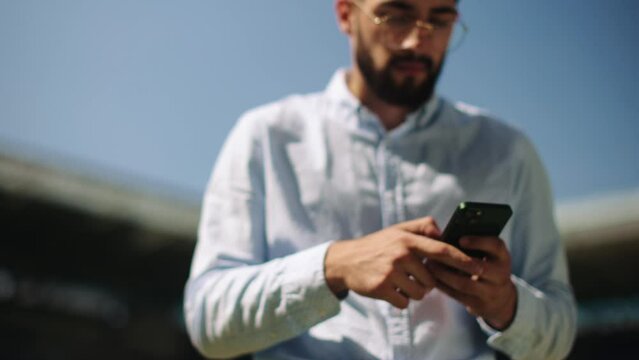 Businessman in formal wear standing on sport stadium, looking on mobile phone, using betting app and winning money. Concept of sport, fan, betting and finances, gambling, bookmaker