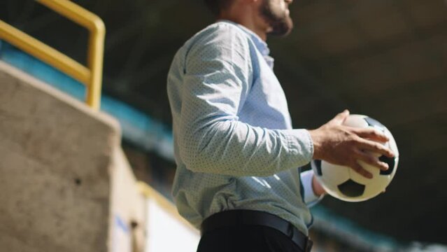Businessman in formal wear standing on sport stadium with football ball, spreading hands in success. Money win. Concept of sport, fan, betting and finances, gambling, bookmaker