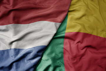 big waving national colorful flag of netherlands and national flag of benin .
