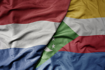 big waving national colorful flag of netherlands and national flag of comoros .