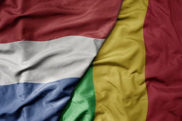 big waving national colorful flag of netherlands and national flag of mali .