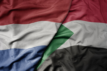 big waving national colorful flag of netherlands and national flag of sudan .