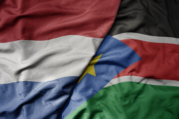 big waving national colorful flag of netherlands and national flag of south sudan .