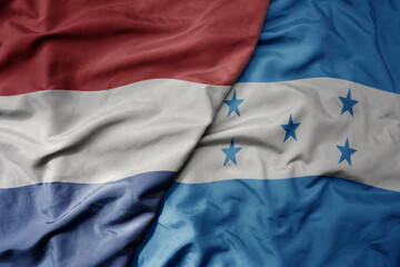big waving national colorful flag of netherlands and national flag of honduras .