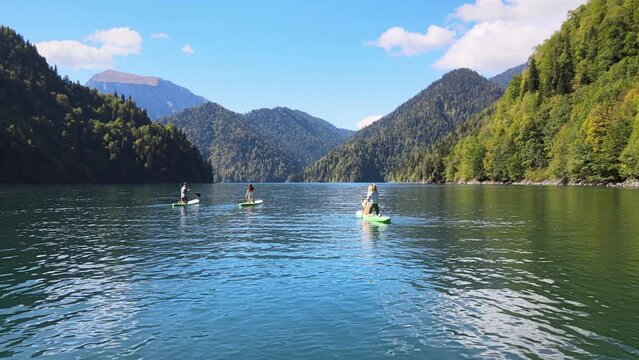 Happy man friends riding on sup board and swims surfing on the lake with a paddle for swimming rowing sport surfer friends close up slow motion. Active sport, fun leisure time. Fantastic mountain view