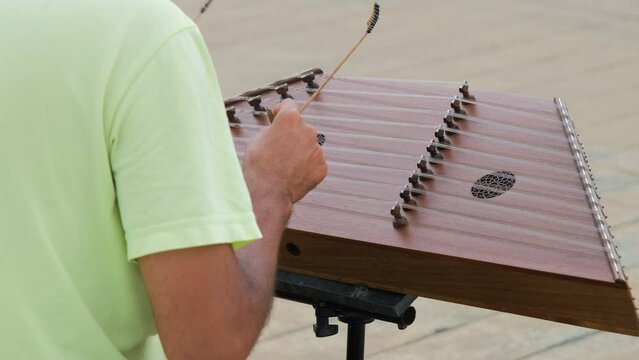 Rear view of male musician playing on santoor, cimbalom or dulcimer outdoors, slow motion 