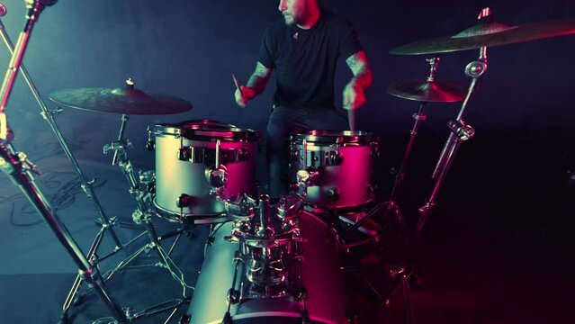 A drummer plays on a dark stage in the fog and neon lights.