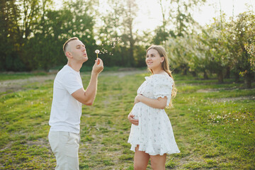 Fototapeta premium Tender romantic pregnant couple hugging in blooming apple spring garden. Expectant parents in the park of white flowering trees. A couple is expecting a baby