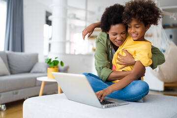 Happy ecstatic African American woman single mother embracing her young daughter in front of laptop...
