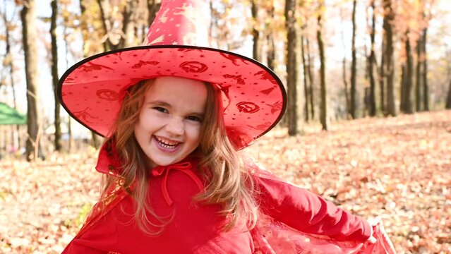 little girl in a Halloween costume and a witch hat scares people and has fun on the background of an autumn forest. Halloween celebration.