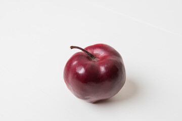 A whole red apple on a white table with a white background.