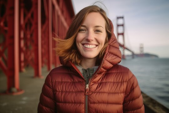 Environmental portrait photography of a grinning girl in her 30s wearing a quilted insulated jacket at the golden gate bridge in san francisco usa. With generative AI technology
