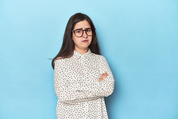 Young Caucasian woman on blue backdrop suspicious, uncertain, examining you.