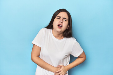 Young Caucasian woman on blue backdrop having a liver pain, stomach ache.