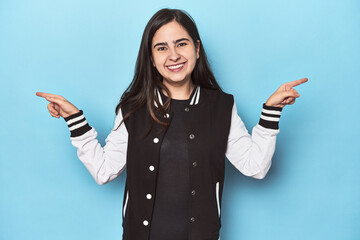 Young Caucasian woman on blue backdrop pointing to different copy spaces, choosing one of them, showing with finger.