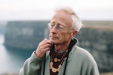 Photography in the style of pensive portraiture of a tender mature man wearing a whimsical charm necklace at the cliffs of moher in county clare ireland. With generative AI technology - obrazy, fototapety, plakaty
