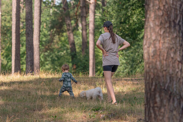 Little boy in overalls. Child on a walk in the park. Happy childhood. A child learns to walk. Back view. Baby and mom. A child in nature.