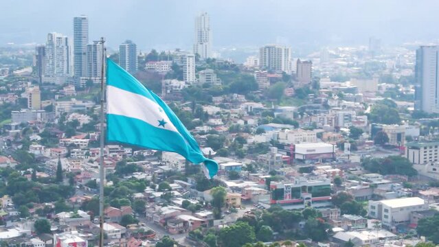 A nice circling footage of Honduran flag and with a cityscape as background and with sunlight illuminating the patriotic symbol 