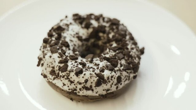 A donut with white icing and chocolate sprinkles rotates on a white plate. Close-up.