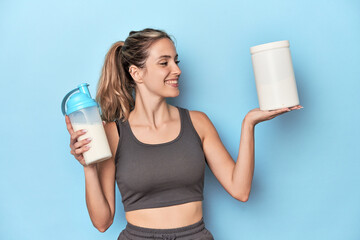 Athlete with protein shake and container in blue studio