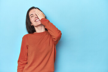 Young caucasian woman on blue backdrop laughing happy, carefree, natural emotion.