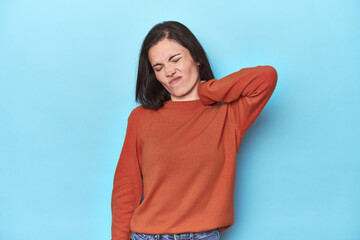 Fototapeta premium Young caucasian woman on blue backdrop suffering neck pain due to sedentary lifestyle.