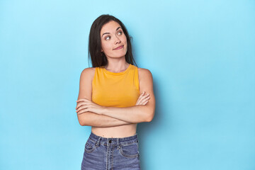 Young caucasian woman on blue backdrop dreaming of achieving goals and purposes