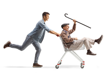 Grandson pushing his grandfather inside a shopping cart - obrazy, fototapety, plakaty