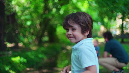 Portrait of small boy at park during bright sunny day. Vibrant green summer afternoon, close-up of child's face turning to camera