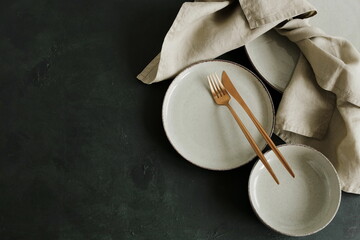 Modern minimal table place setting neutral beige color on dark textured background top view with copy space. Modern kitchen.Scandinavian style tableware.Business food brand template.