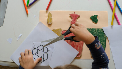 Little girl making poster of garbage containers for sorting at kindergarten or primary school. Recycling education concept.