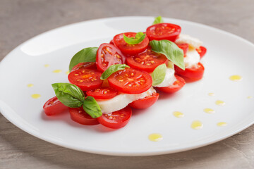 A view of caprese salad with tomatoes, mozzarella, basil and olive oil on white plate on dark table. Isometric style. Mediterranean cuisine. Selective focus.