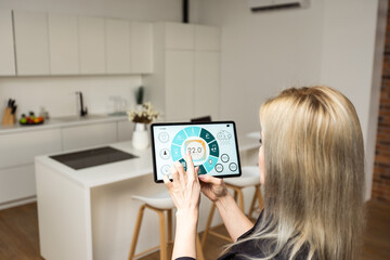 Fototapeta na wymiar Woman pushing button on kitchen app of smart home on digital tablet at home. Concept of modern home control. Idea of domestic lifestyle. Cropped image of girl. Blurred man on background using laptop.