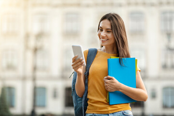 Smiling Young Female Student With Smartphone And Workbooks Relaxing Outdoors