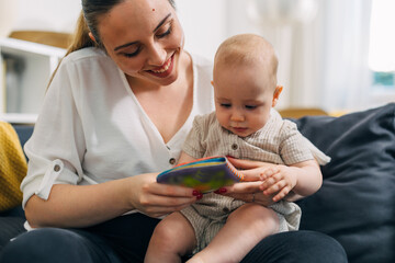 Cheerful mother is showing a child’s book to her baby.