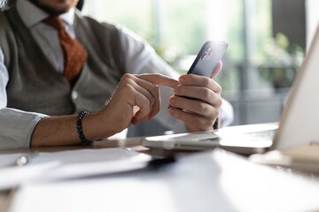 Closeup view of male hands touching mobile phone. Middle-aged man using smartphone while sitting at...