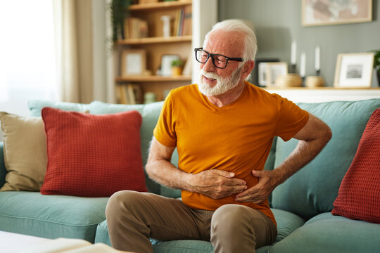 Senior man suffering from stomach ache sitting on a couch in the living room at home