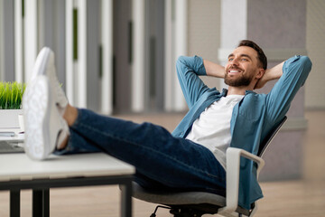 Break At Work. Young man relaxing at desk with legs on table