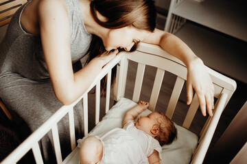 The child sleeps in a crib, the mother sits next to her and tenderly looks at her daughter