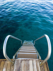 Deep blue water around pier or dock with metal handrail. Swimming, jumping into sea or ocean, diving or snorkeling concept.