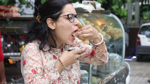 Happy Indian woman having North Indian subcontinent popular street food. Hand cracking panipuri. Street food. Appetizer.