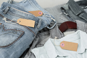 Stack of blue jeans, shirts and empty tag. Second hand clothing shop. Circular fashion, eco...