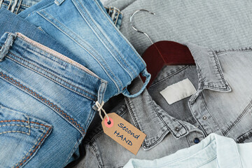 Stack of blue jeans, shirts and tag with inscription second hand. Second hand clothing shop....